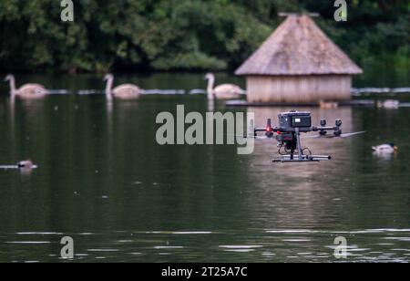 17 ottobre 2023, Meclemburgo-Pomerania occidentale, Rostock: Un drone con sonde per rilevare campi magnetici o anomalie sul fondo del lago vola sopra lo stagno dei cigni durante i voli di misurazione. Le immagini possono essere utilizzate per identificare e individuare eventuali ordigni nel fango. Dal momento che lo stagno è stato creato nel 1938 prima della seconda guerra mondiale, vi è il sospetto di contaminazione da ordigni esplosivi. Foto: Jens Büttner/dpa Foto Stock