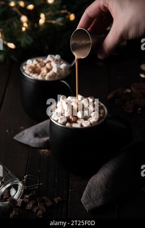 Irish Cream Liquour viene versato nella cioccolata calda festosa. Foto di cioccolata calda a tema natalizio condita con mini marshmellows e spolverata di cioccolato Foto Stock