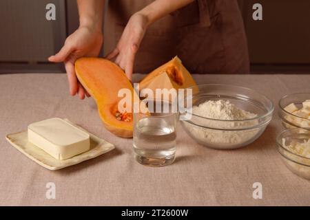 ricetta di zucca al forno per cucinare in casa. la cuoca donna in grembiule marrone da cucina tiene la zucca a fette Foto Stock