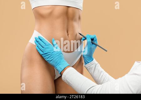 Il medico disegna segni sullo stomaco femminile, preparandosi per l'operazione di chirurgia estetica Foto Stock