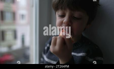 Bambino che mangia fragole dalla finestra. Bambino che prende un morso di frutta sana e nutriente Foto Stock