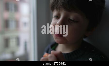 Bambino che mangia fragole dalla finestra. Bambino che prende un morso di frutta sana e nutriente Foto Stock