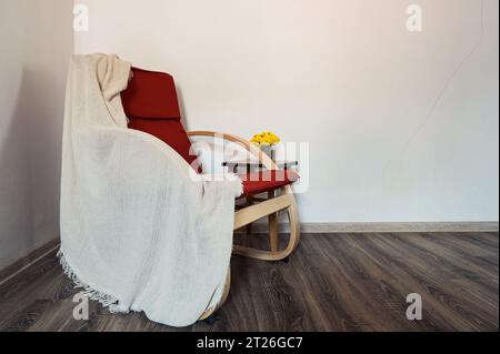 Poltrona moderna in legno e fiori gialli su un piccolo tavolo vicino ad esso. Arredamento, stile Foto Stock