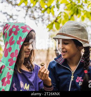 Ragazze avventuriere multietniche in abiti casual accovacciati nella natura selvaggia guardando un pezzo di ghianda - ambiente e concetto di amanti della natura Foto Stock