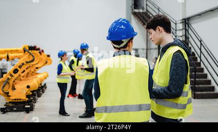 Ingegneri che monitorano il braccio robotizzato presso un magazzino robotizzato, persone che lavorano nel settore dell'intelligenza artificiale industriale Foto Stock