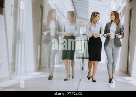 Due belle giovani donne d'affari che camminano e discutono nel corridoio dell'ufficio Foto Stock
