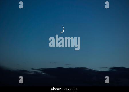 Madrid, Spagna. 18 ottobre 2023. Luna crescente cerata vista di sera dopo il tramonto e circondata da cielo blu e nuvole scure Foto Stock