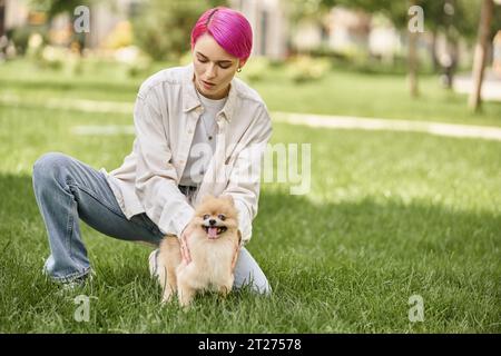 elegante donna dai capelli viola con adorabile spitz della pomerania sul prato verde del parco, attività all'aperto Foto Stock