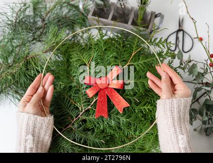 Il concetto di prepararsi per Natale e Capodanno. Una ragazza fa una corona di Natale, il processo di creare una corona di Natale con aghi di pino, thuj Foto Stock