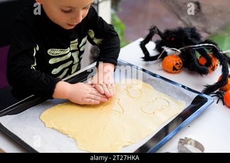 ragazzo vestito da scheletro che prepara biscotti di halloween a casa. Prepariamo halloween Foto Stock