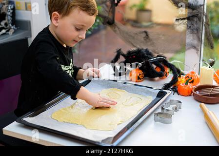 ragazzo vestito da scheletro che prepara biscotti di halloween a casa. Prepariamo halloween Foto Stock