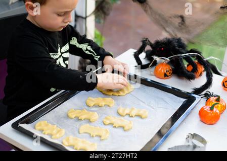 ragazzo vestito da scheletro che prepara biscotti di halloween a casa. Prepariamo halloween Foto Stock