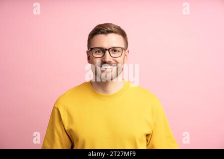Uomo contento sorridente, ritratto su una parete da studio rosa. Un ragazzo istruito e professionale intelligente guarda la fotocamera Foto Stock