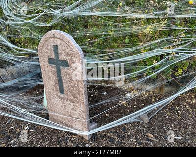 Una grande lapide con una croce è in un cortile. Il cortile e la lapide sono ricoperti da ragnatele. Questo è per celebrare Halloween. Foto Stock