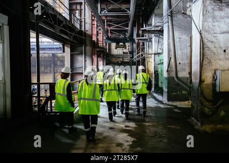 Gruppo di lavoratori in uniforme che cammina lungo il corridoio della fabbrica. Foto Stock