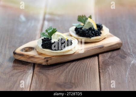Caviale di storione nero su pancake su un piatto di legno da vicino Foto Stock