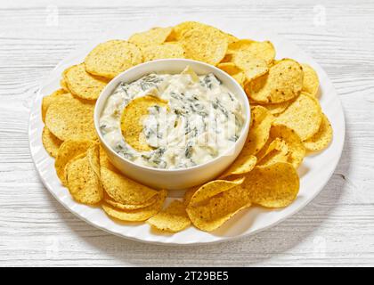 salsa cremosa di carciofi spinaci alle mandorle con patatine fritte su piatto bianco su un tavolo di legno bianco, vista orizzontale dall'alto, primo piano Foto Stock