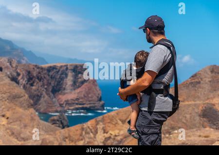 Un padre con il suo bambino nello zaino a Ponta de Sao Lourenco che guarda il paesaggio e il mare, Madeira Foto Stock