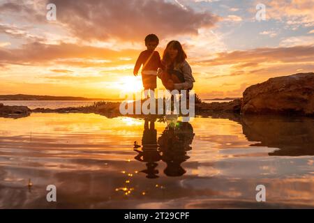 Tramonto a Ibiza in vacanza, una madre con suo figlio sul mare a San Antonio Abad, che lancia pietre Foto Stock