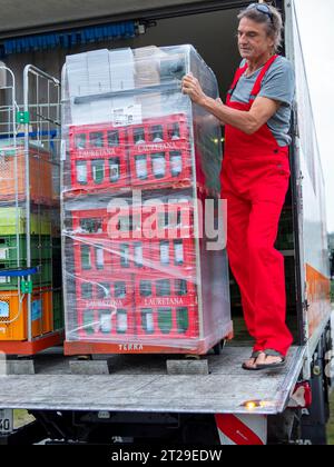 Uomo su rampa di carico camion, consegna con prodotti biologici e scatole di acqua in carrelli, fornitura al dettaglio e trasporto commercio biologico, Germania Foto Stock