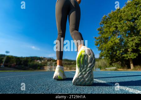 Vista ravvicinata e ad angolo elevato di una suola da running flexata di una velocista femminile in tights da running che si prepara a iniziare una gara su un trac da running blu Foto Stock