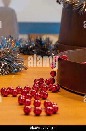 Ghirlande di perle rosse metalliche e tinsel argento su un tavolo di legno. Decorazione natalizia pronta per decorare la casa. Messa a fuoco selettiva Foto Stock