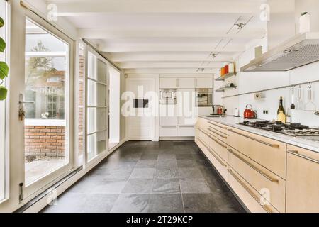 Interno di una spaziosa cucina con ripiani bianchi e armadi in una casa moderna con grandi finestre e pavimenti piastrellati Foto Stock