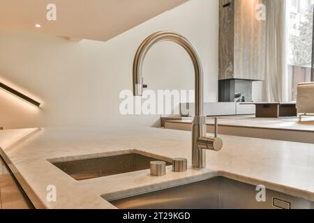Interno della cucina con ripiano in marmo bianco, lavandino e rubinetto in acciaio inox in un moderno appartamento luminoso Foto Stock