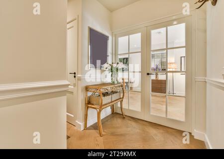 Vaso di fiori su tavolo di legno con specchio su parete bianca da grandi porte chiuse nel corridoio di un appartamento moderno Foto Stock