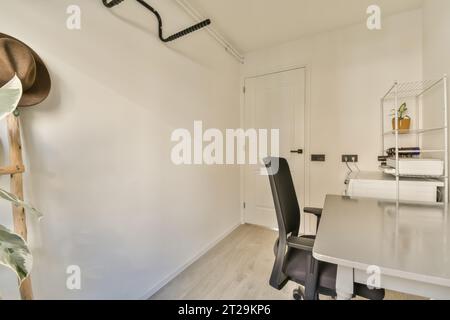 Interno di un piccolo ufficio domestico con scrivania pulita e sedia vuota con pareti bianche in un appartamento luminoso Foto Stock