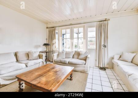 Comodi divani bianchi con tavolino da caffè in legno collocati da una grande finestra in un luminoso soggiorno in una casa contemporanea Foto Stock