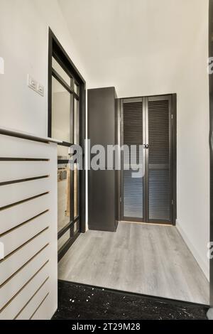 Interno di un corridoio vuoto con porte nere chiuse e parete bianca in una moderna casa luminosa Foto Stock