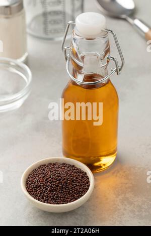 Bottiglia con olio di senape marrone e una ciotola di vetro con semi di senape nera davanti da vicino Foto Stock