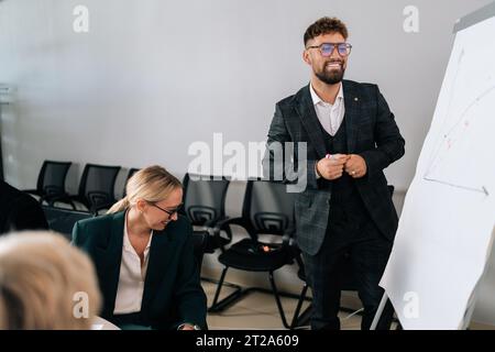 Ritratto di un dirigente d'affari positivo che guida una riunione d'affari, presenta una lavagna a fogli mobili, formazione di un gruppo di lavoro di consulenza. Foto Stock