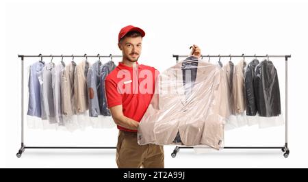 Un lavoratore di pulitura a secco che tiene un vestito in una custodia di plastica davanti agli abiti appesi a un rack isolato su uno sfondo bianco Foto Stock