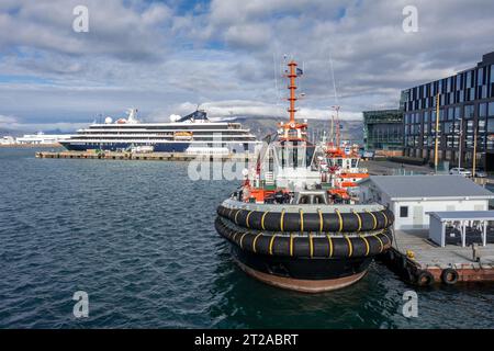 Atlas Ocean Voyages World Traveller, piccola nave da crociera in stile yacht a Port Reykjavik, Islanda, con rimorchiatori fuori dall'Harpa Centre Foto Stock