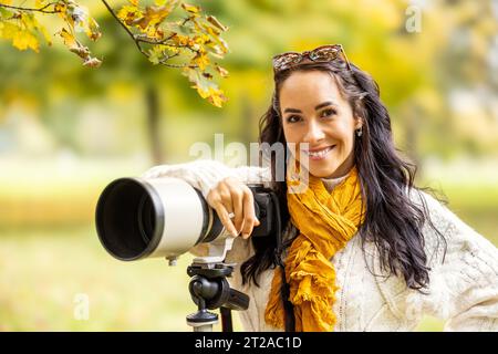 Una fotografa professionista si trova accanto alla sua fotocamera, scattando foto di ritratti o paesaggi autunnali. Foto Stock