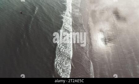 Vista aerea minimalista delle onde dell'oceano che si infrangono su una spiaggia sabbiosa Ripresa aerea con droni ad angolo alto che guarda verso il basso le dolci onde dell'oceano e la schiuma bianca del mare che si riversa Foto Stock