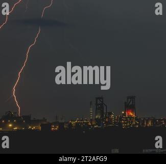 Un fulmine luminoso lampeggia nel cielo notturno, illuminando la raffineria industriale sottostante Foto Stock