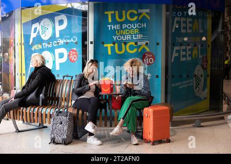 Un paio di donne di mezza età che navigano sui loro smartphone mentre mangiano il fast food McDonalds sedute all'interno di Waterloo Station, Londra, Regno Unito Foto Stock