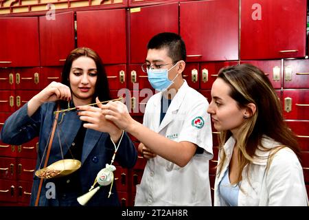 (231018) -- JINAN, 18 ottobre 2023 (Xinhua) -- uno studente iraniano (1st L) del College of International Exchange della Shandong University of Science and Technology impara a pesare i materiali della medicina tradizionale cinese in un ospedale di medicina tradizionale cinese della nuova area di Xihai'an (costa occidentale) a Qingdao, nella provincia dello Shandong della Cina orientale, 18 ottobre 2023. L'ospedale, in collaborazione con il College of International Exchange della Shandong University of Science and Technology, ha invitato gli studenti internazionali dei paesi partner Belt and Road Initiative (BRI) a sperimentare il fascino Foto Stock