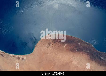 Dalla stazione spaziale Internazionale a 260 miglia di altitudine, il sole risplende al largo del Mar Mediterraneo in contrasto con la costa desertica della Libia. Bengasi, una città di 1,2 milioni di abitanti, si trova nella regione arida tra il deserto e i climi temperati. Immagine acquisita il 4 agosto 2023. Foto Stock