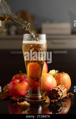 Il sidro di mele viene versato in vetro alto. Bevanda fresca con mele, cannella e anice su sfondo nero. Foto Stock