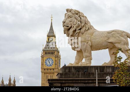 Primo piano di una grande statua di leone in pietra con la torre del Big Ben e l'orologio sullo sfondo, Central London England UK Foto Stock