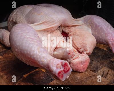 Primo piano con tagliere di legno crudo di pollo intero crudo Foto Stock