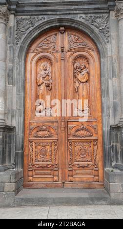 Otavalo, Imbabura / Ecuador - 14 ottobre 2023: Dettaglio della porta principale in legno con incisioni di santi e angeli della chiesa di El Jordan Foto Stock