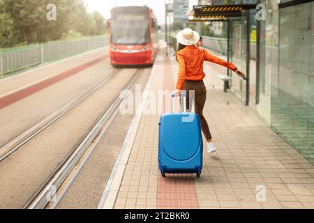 Giovane donna con una valigia che corre per prendere il tram in città Foto Stock