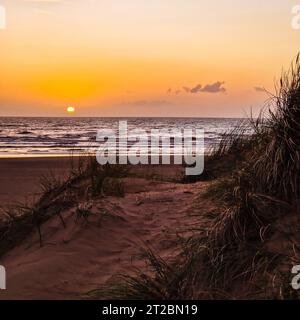 Il sole scende sotto l'orizzonte, proiettando un bagliore dorato su Formby Beach. Foto Stock