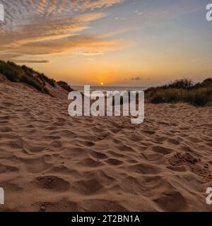 Il sole scende sotto l'orizzonte, proiettando un bagliore dorato su Formby Beach. Foto Stock