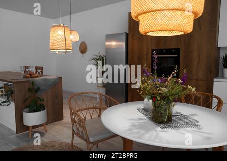 Interno di una cucina moderna con lampade luminose e vaso di fiori sul tavolo da pranzo Foto Stock